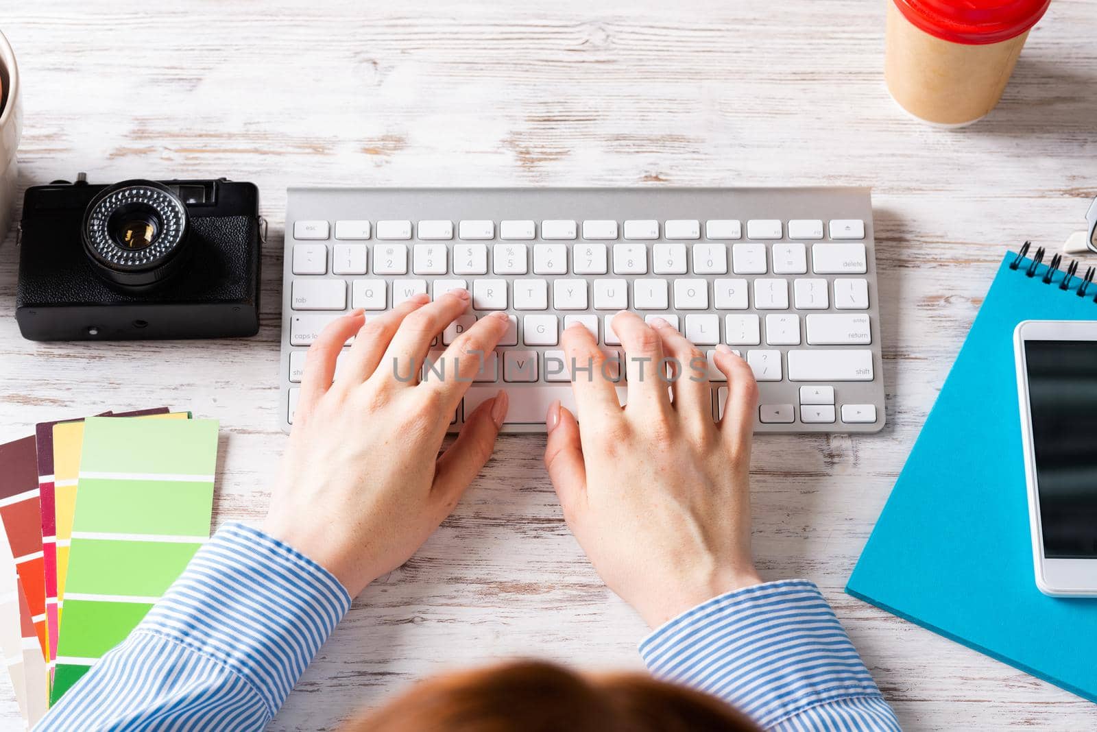 Freelancer sitting at desk and typing on keyboard. Business occupation and innovation. Office workplace with camera, notebook and disposable cup of coffee. Woman blogger work at wooden desk.