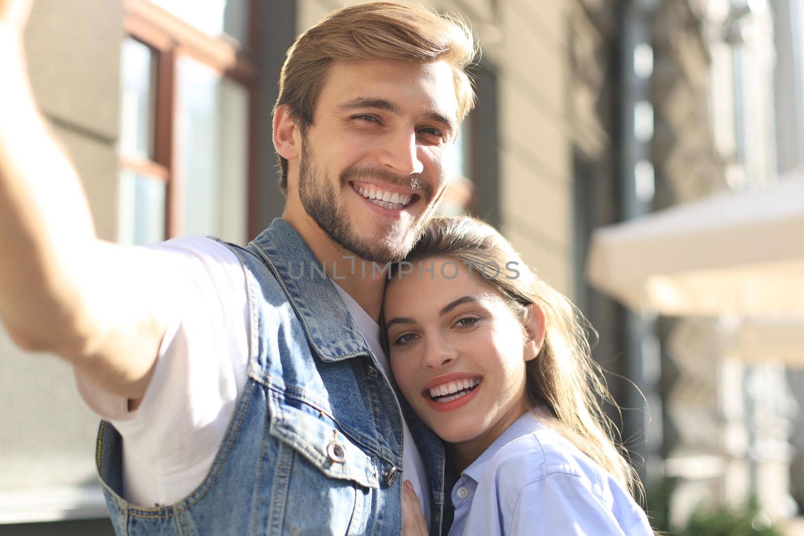 Beautiful lovely young couple walking at the city streets, hugging while taking a selfie