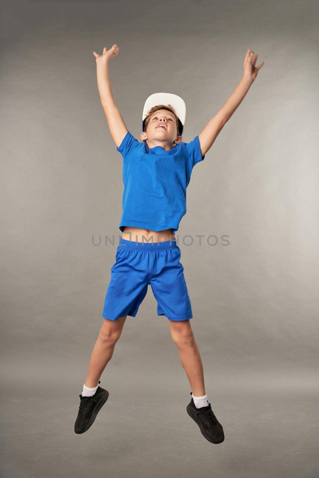 Adorable male child jumping against gray background by friendsstock