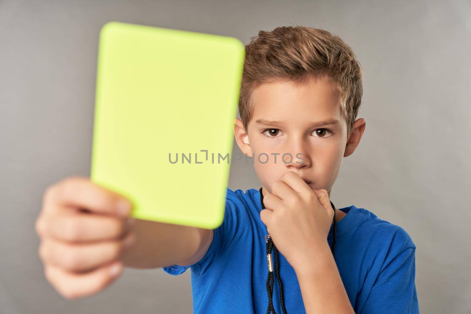 Cute boy referee holding yellow card and whistling in whistle by friendsstock