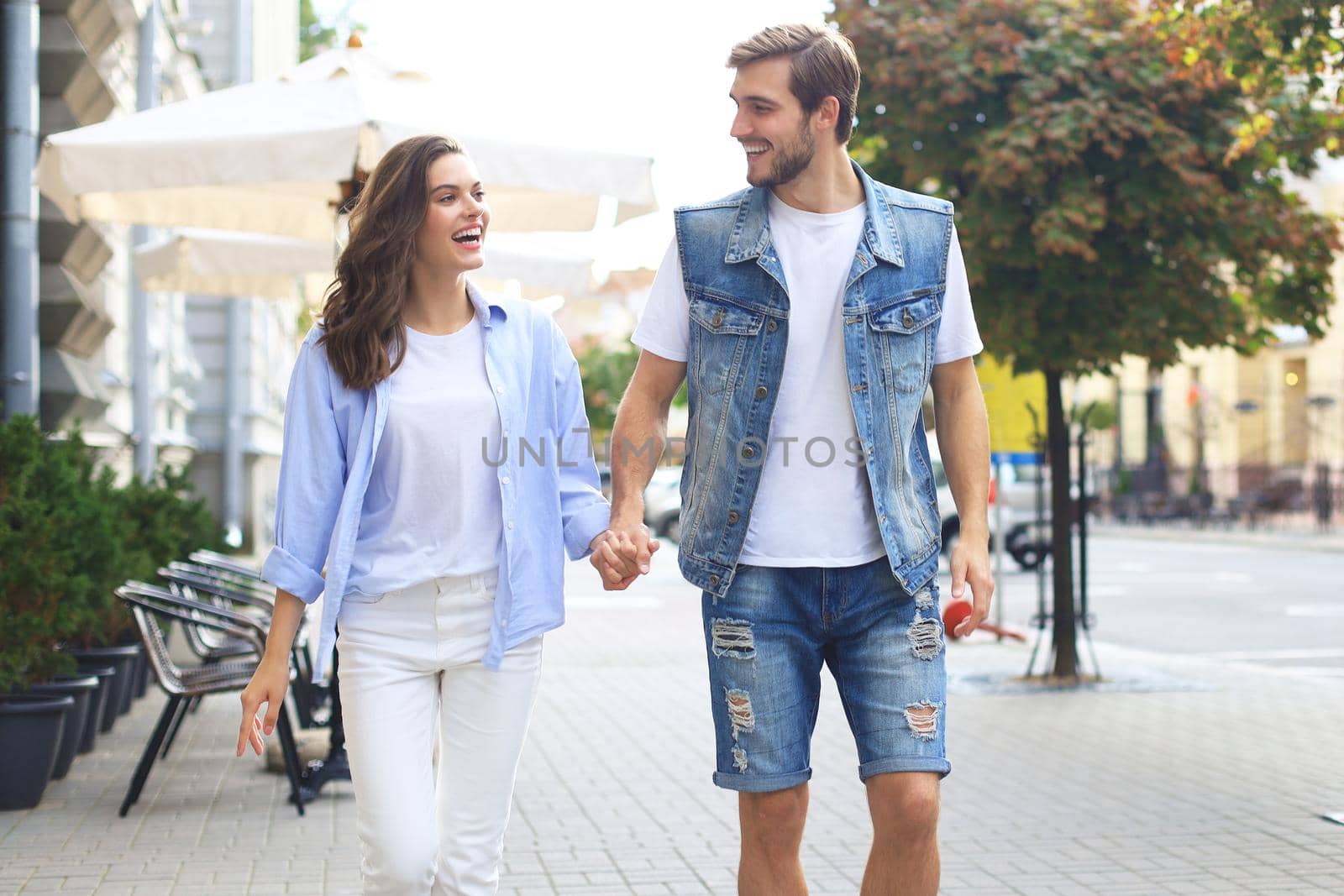 Image of lovely happy couple in summer clothes smiling and holding hands together while walking through city street. by tsyhun