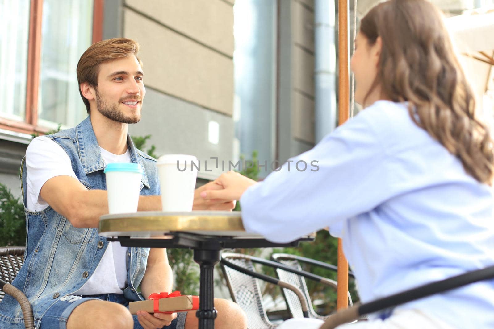 Smiling young girl having a date with her boyfriend at the coffee shop, man holding present box