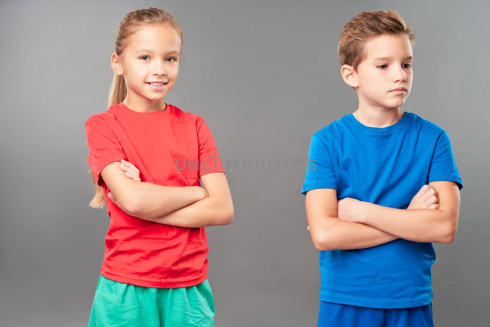 Adorable female child looking at camera and smiling while serious boy crossing arms over his chest