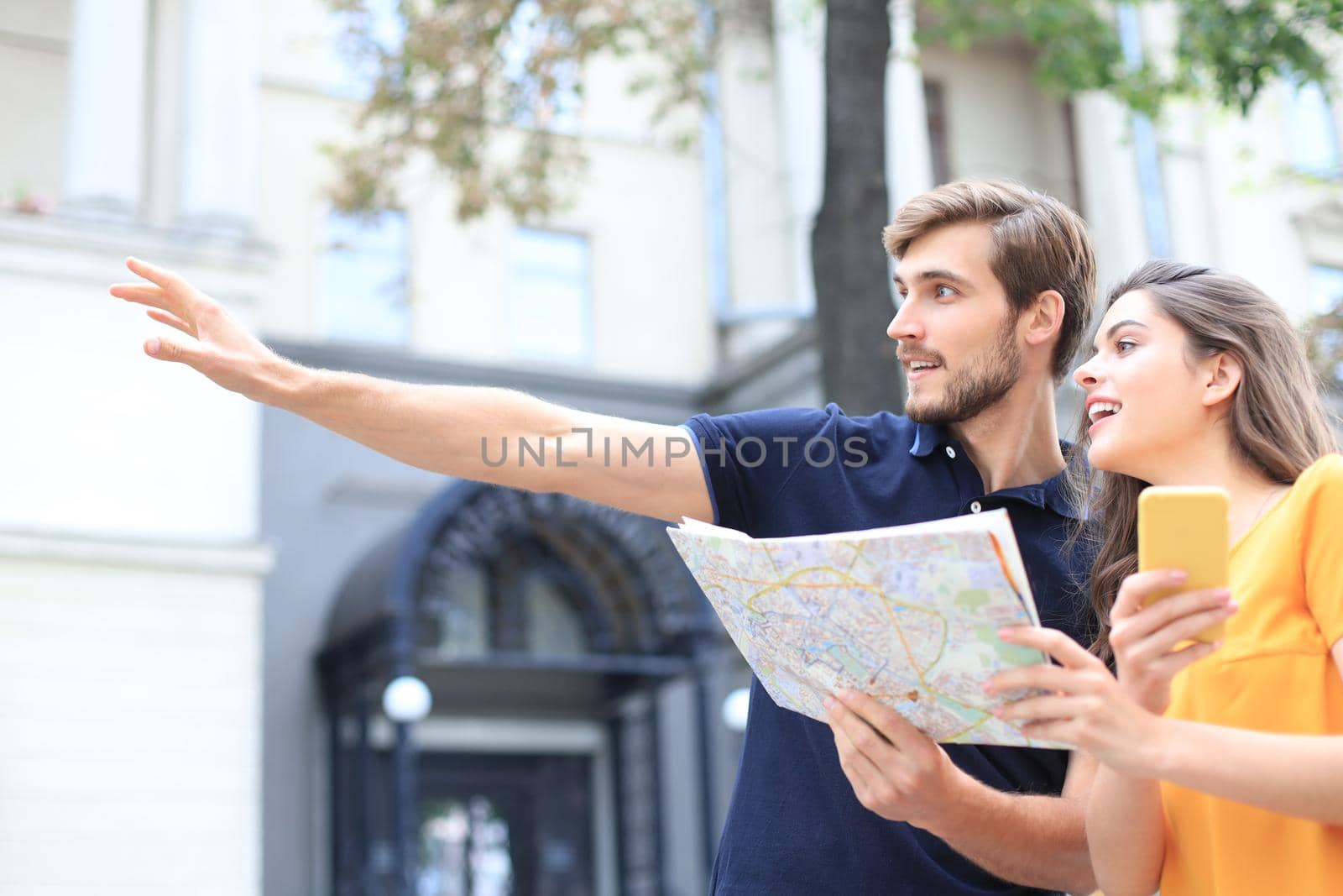 Beautiful young couple holding a map and smiling while standing outdoors. by tsyhun