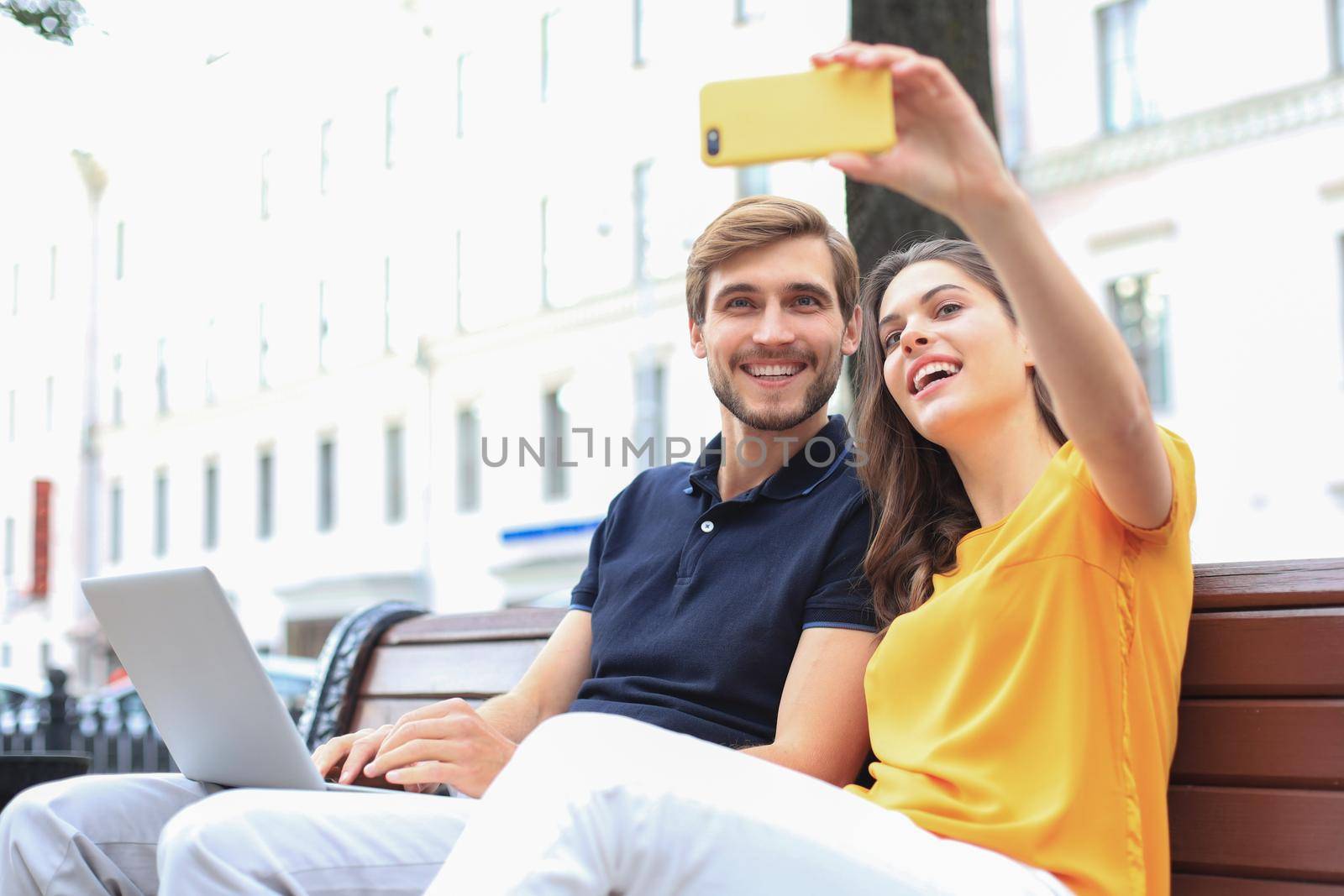 Attrative young couple sitting on a bench and taking selfie on smartphone