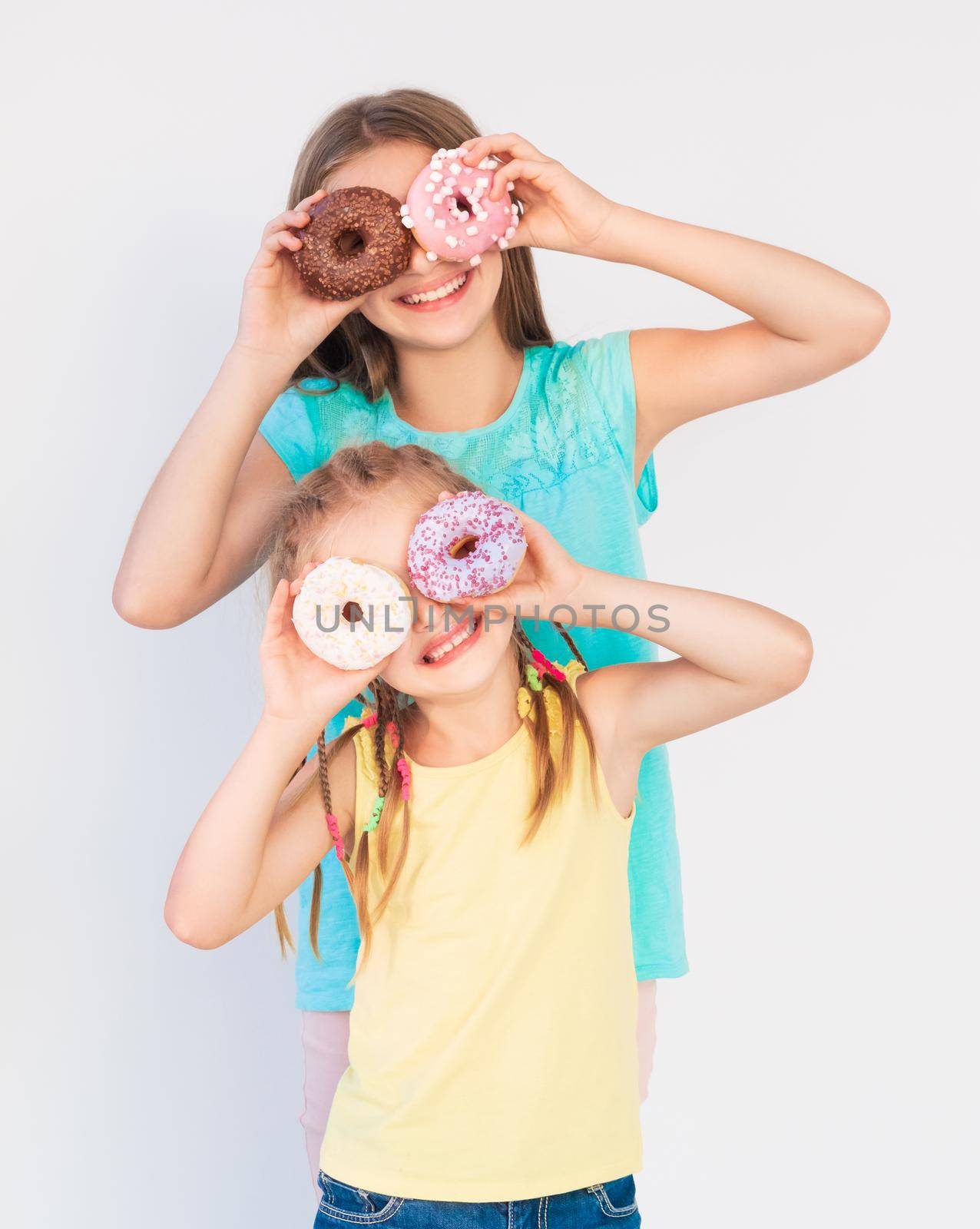 Two girls making funny jokes and joyful expressions using freshly baked donuts