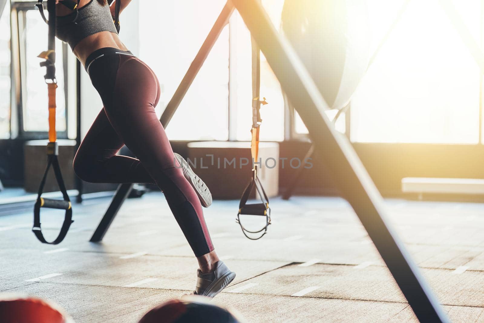 Cropped shot of a fitness woman with beautiful slim body wearing sports clothes exercising with fitness trx straps at gym. Sport, workout, wellness and healthy lifestyle