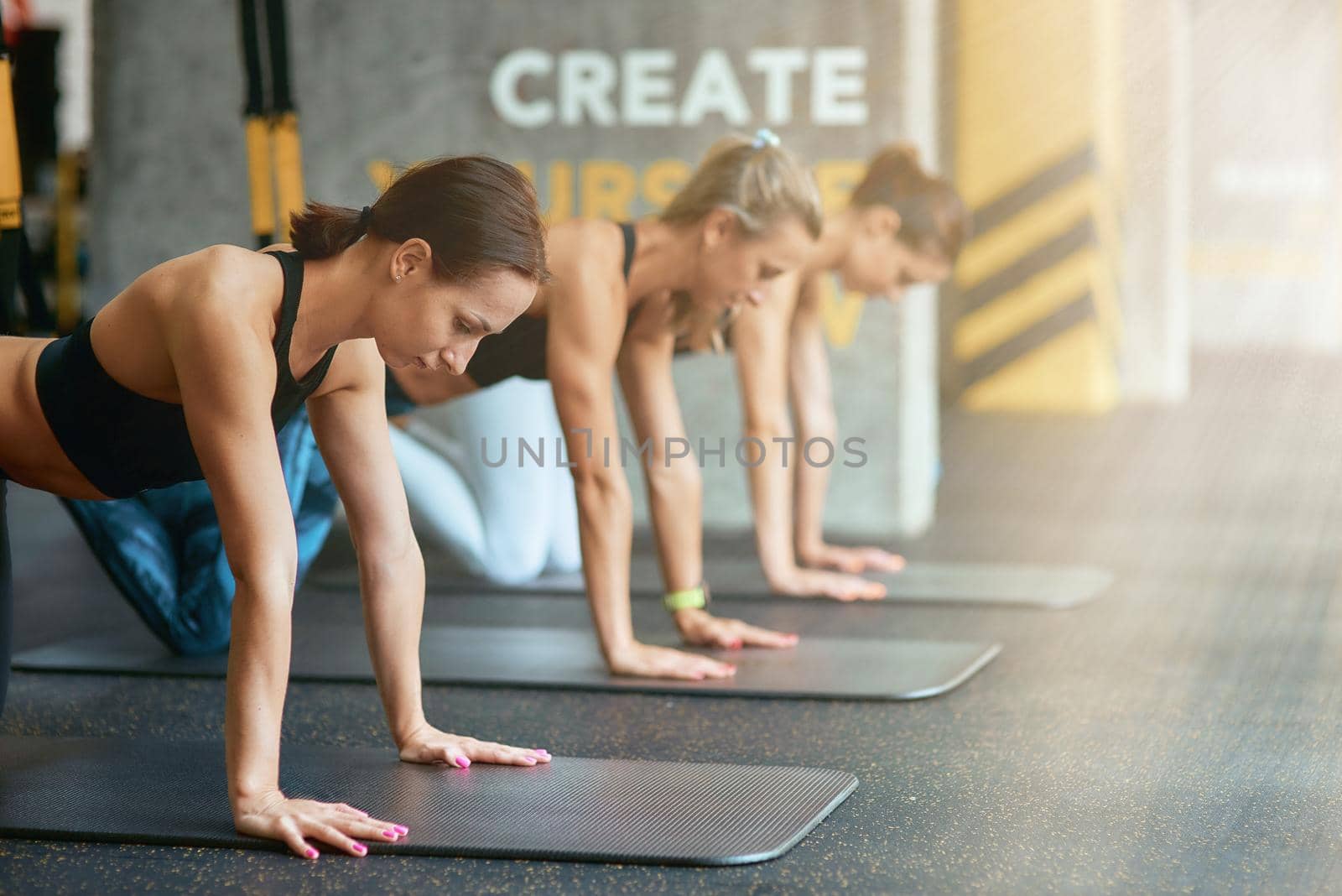 Create yourself. Group of three young sportive women exercising with trx fitness straps at gym. Suspension training, workout, wellness and healthy lifestyle