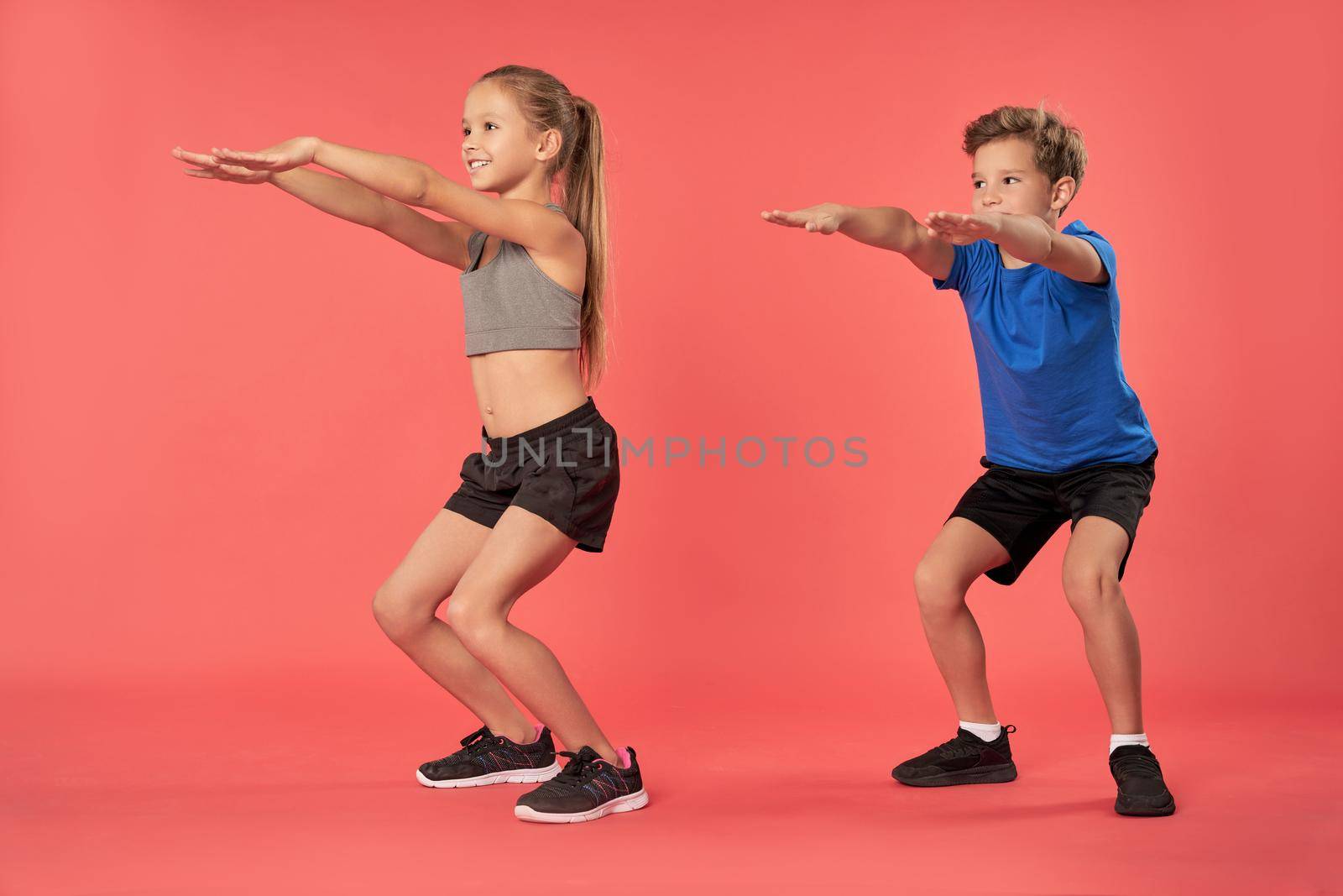 Cheerful sporty kids looking away and smiling while doing exercise. Isolated on red background