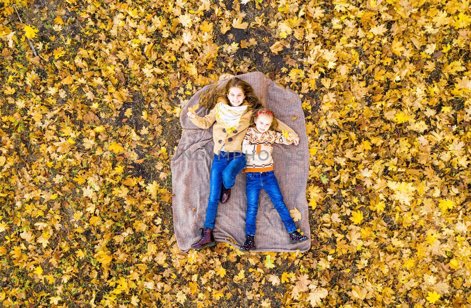 Happy girls lying on picnic mat in autumn park, aerial view
