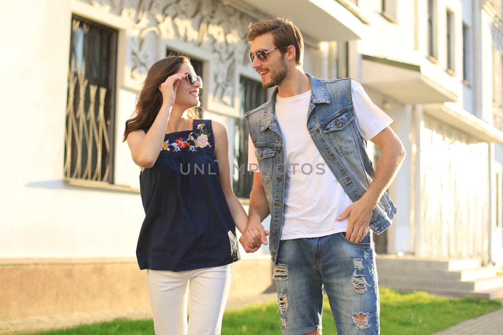 Image of lovely happy couple in summer clothes smiling and holding hands together while walking through city street