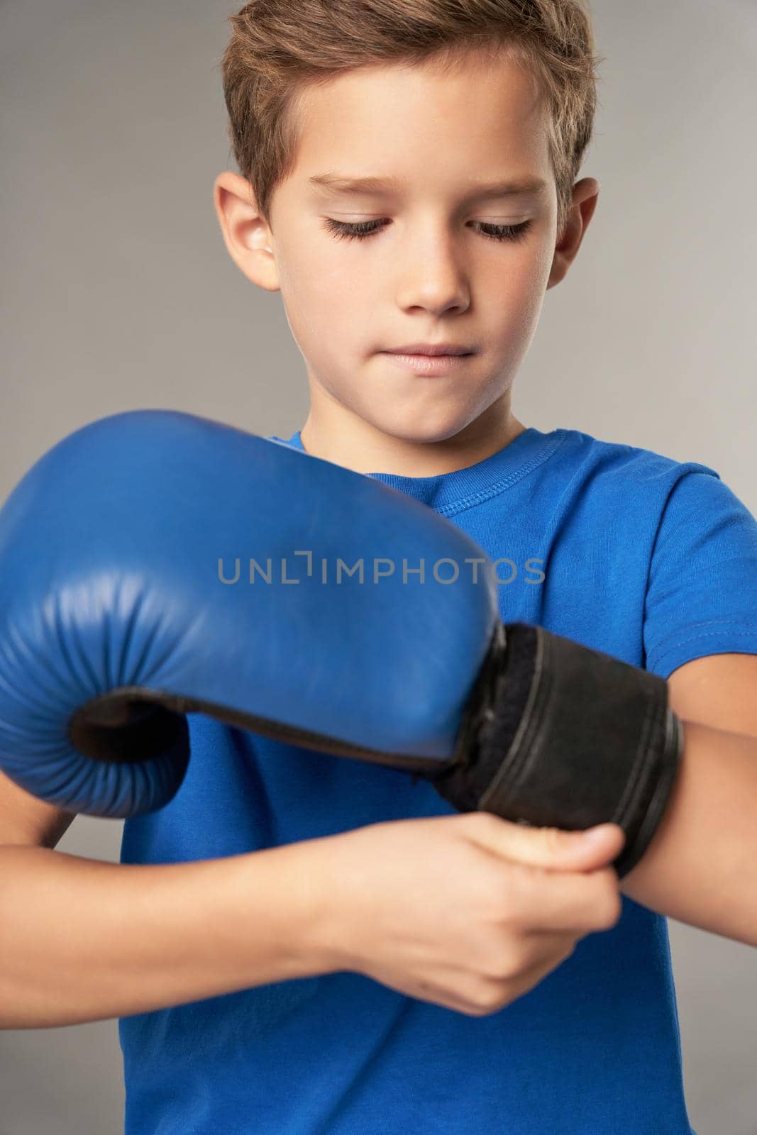 Cute boy putting on boxing gloves against gray background by friendsstock