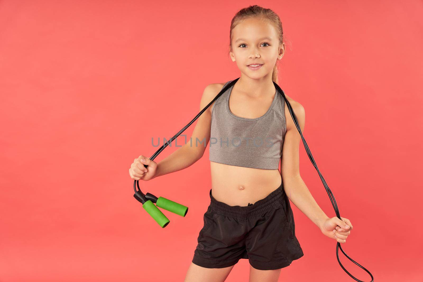 Cute girl with skipping rope standing against red background by friendsstock