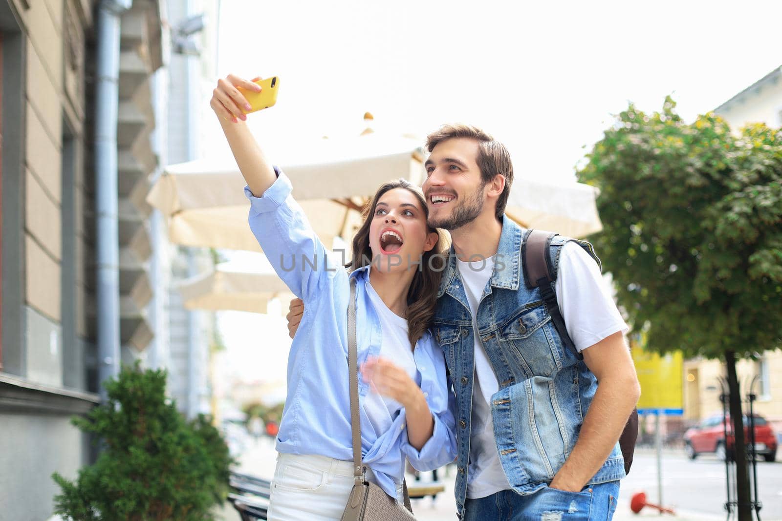 Beautiful lovely young couple walking at the city streets, hugging while taking a selfie