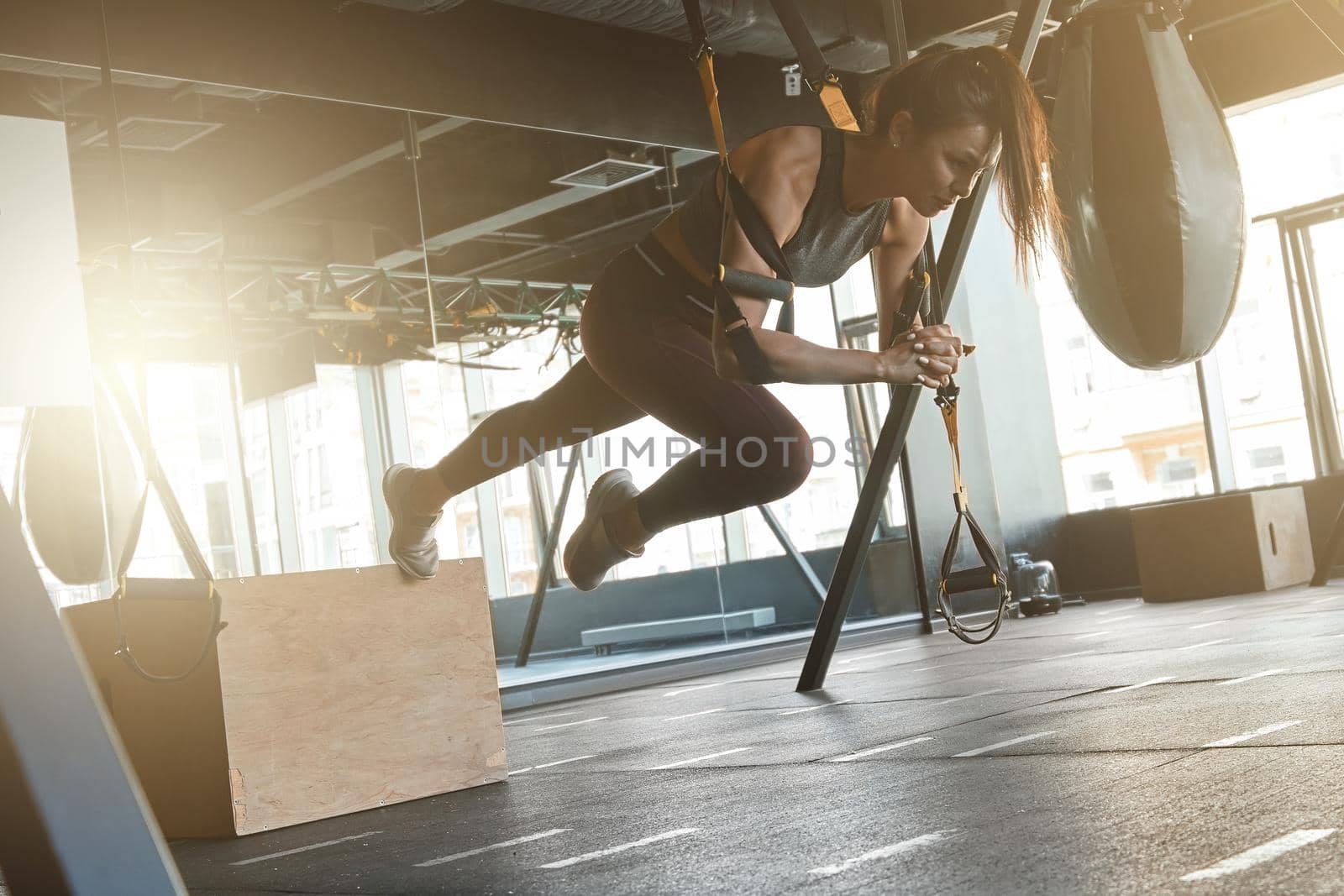 Pushing The Limits. Young athletic strong woman in sportswear doing TRX workout at industrial gym, exercising with fitness straps. Suspension training concept. Sport, wellness and healthy lifestyle