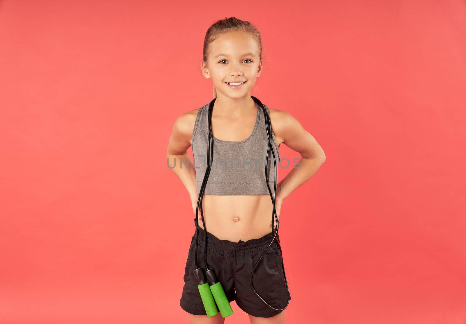 Cute female child with jump rope looking at camera and smiling while wearing sports shorts and crop top