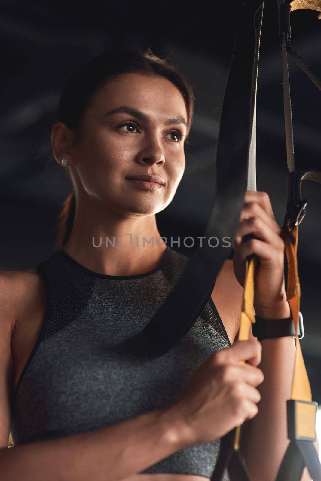 Workout. Vertical shot of a young attractive woman holding trx fitness straps while exercising at industrial gym by friendsstock