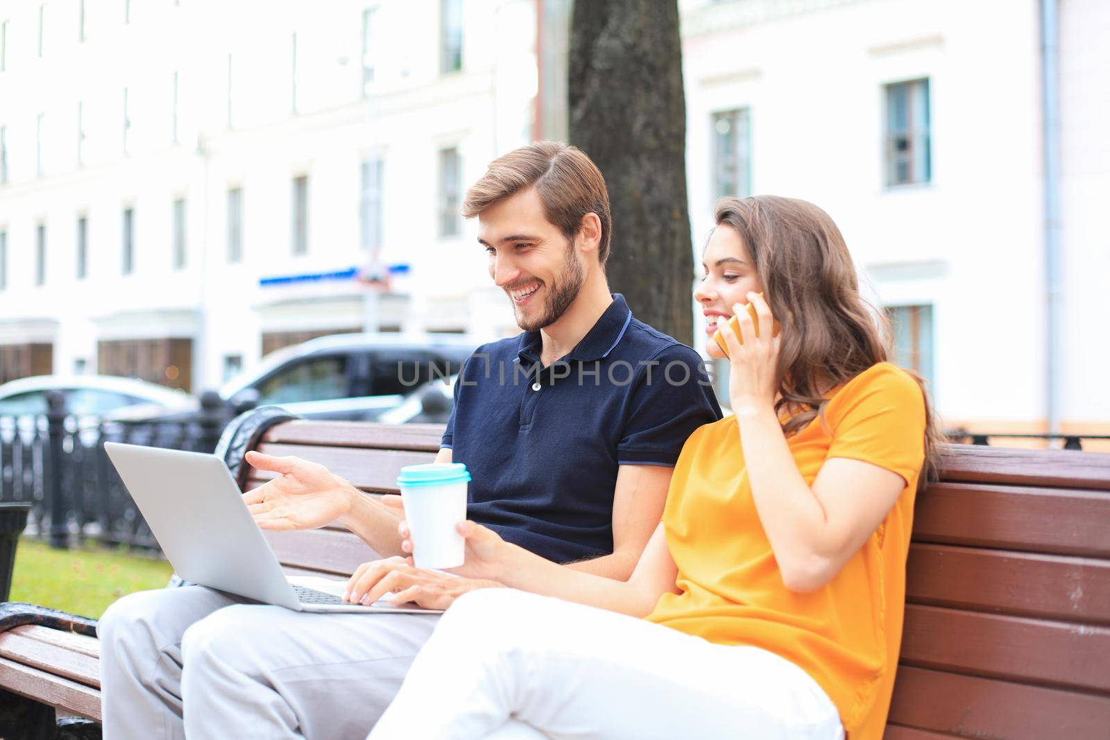Attrative young couple using laptop computer while sitting on a bench outdoors. by tsyhun