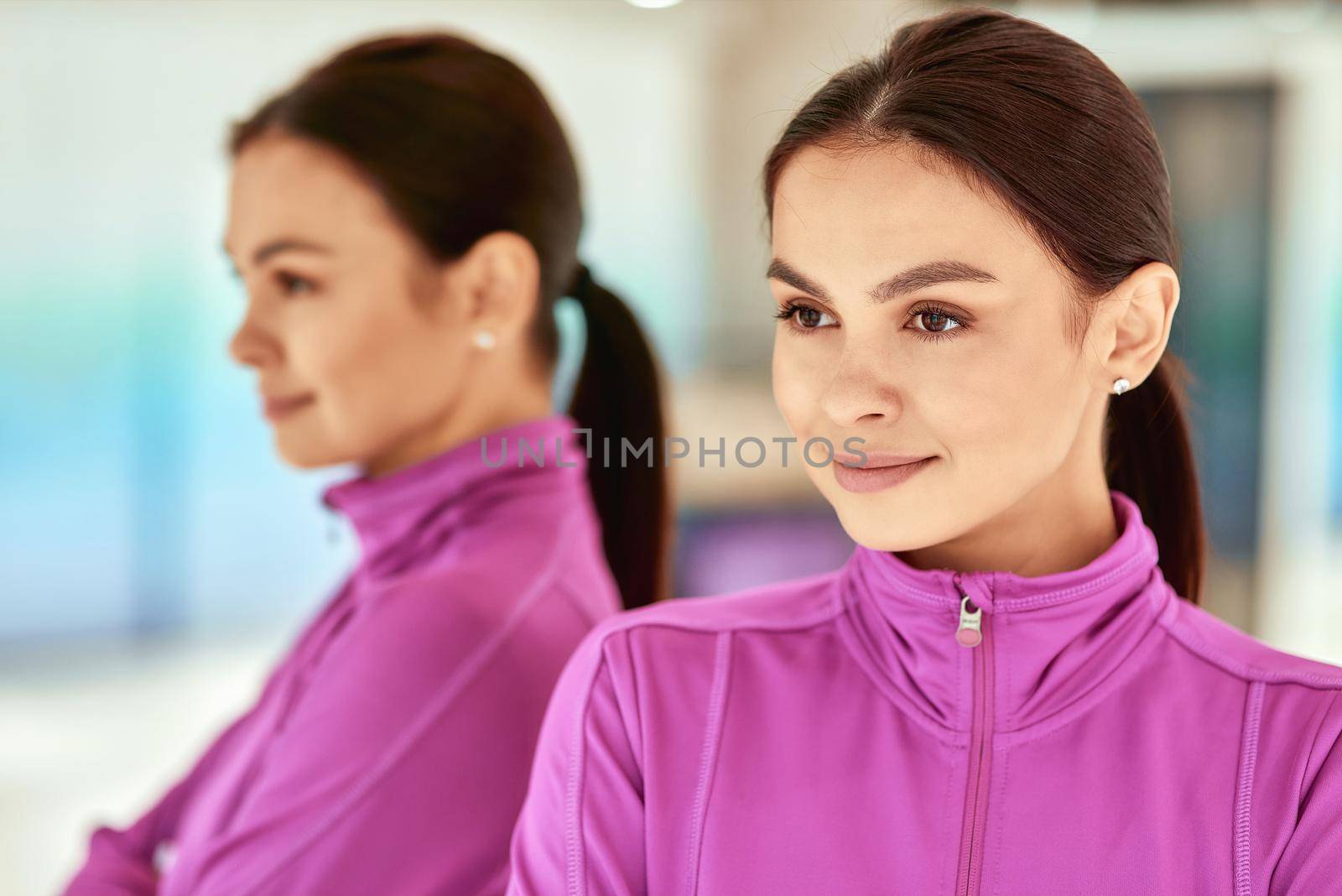Portrait of a young beautiful caucasian woman in sportswear standing in studio or gym against mirror and looking away. Sport, wellness and healthy lifestyle