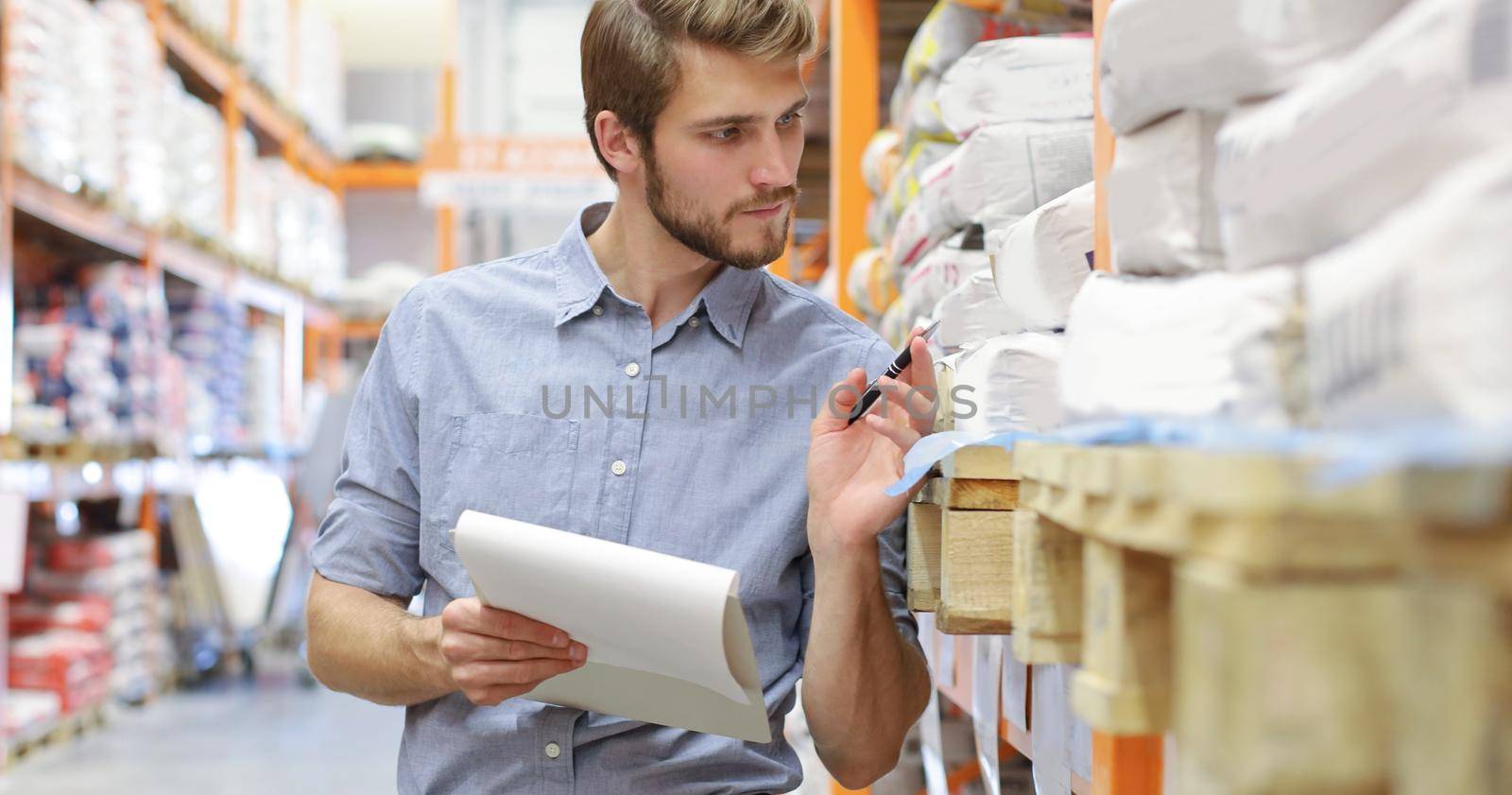 Young man shopping or working in a hardware warehouse standing checking supplies on his tablet