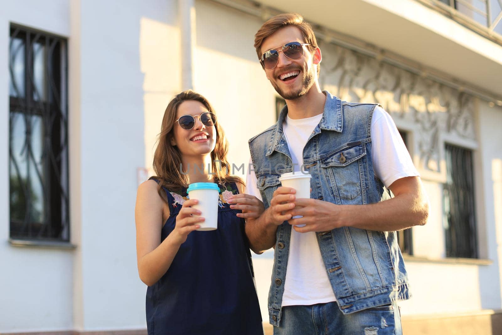 Beautiful young couple walking through the city street, smiling and drinking coffee from paper cup