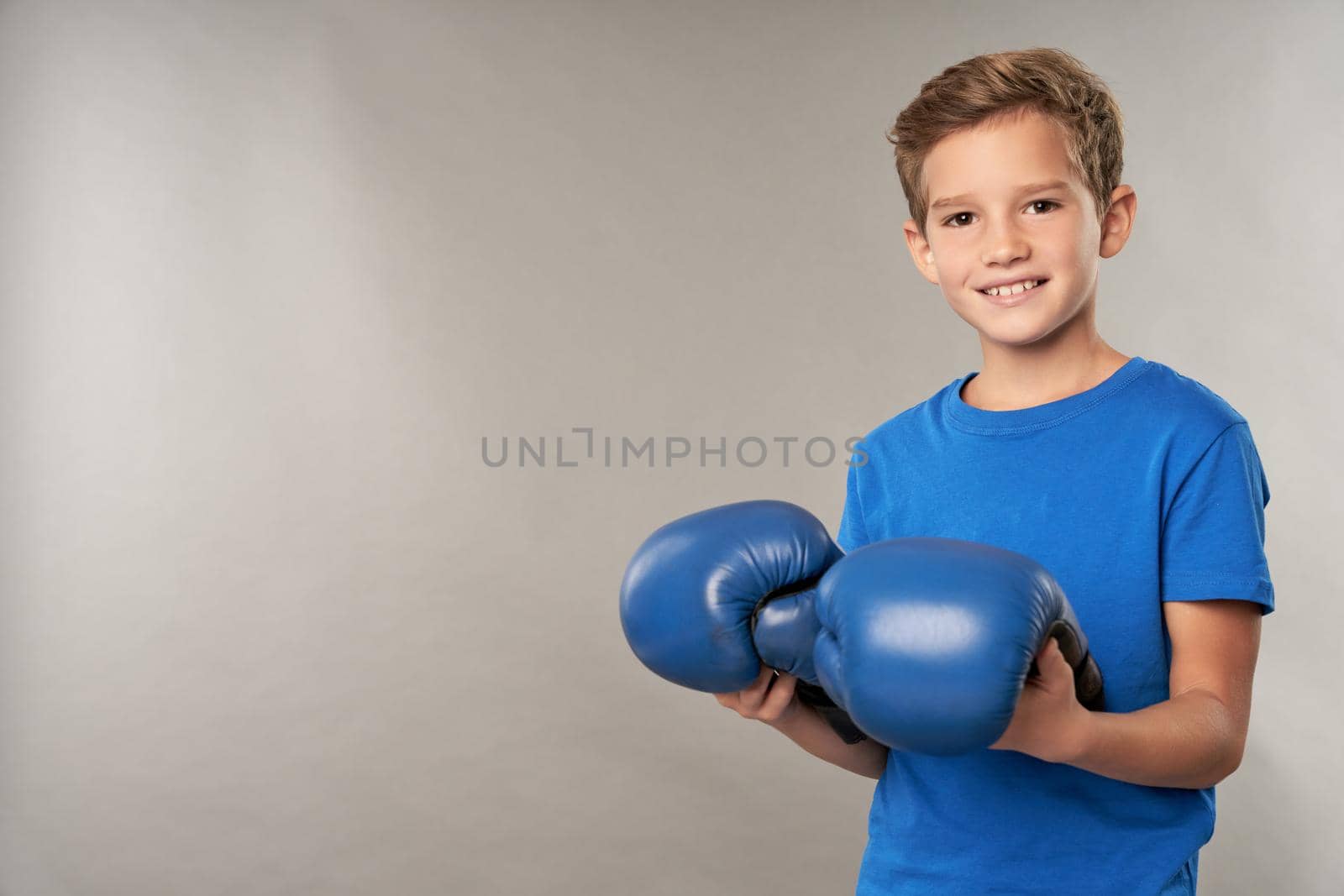 Joyful boy with boxing gloves standing against gray background by friendsstock