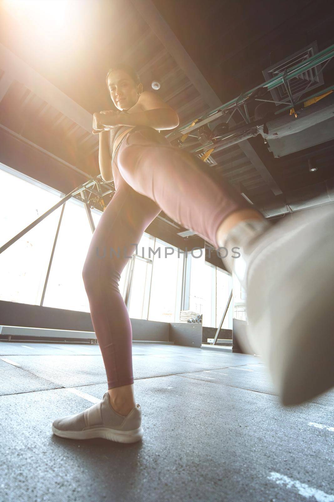 Bottom view of athletic woman in sportswear kicking with the leg while working out at industrial gym, warming up before training by friendsstock