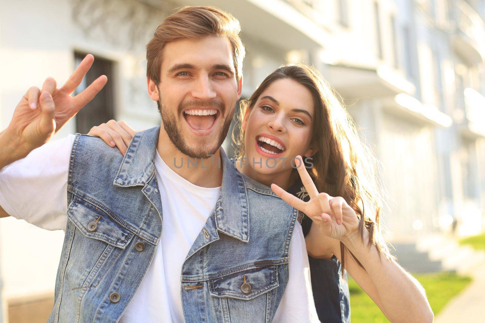 Image of a happy smiling cheerful young couple outdoors take a selfie by camera showing peace