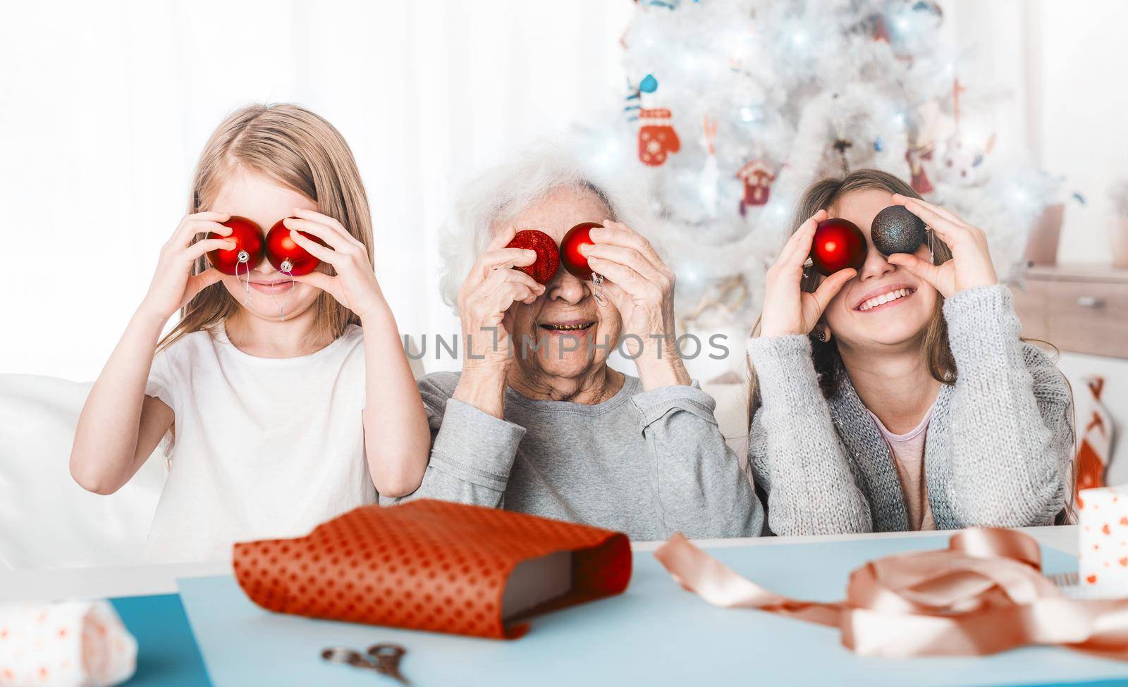 Smiling granddaughters holding decorative balls like eyes with grandma at Christmas