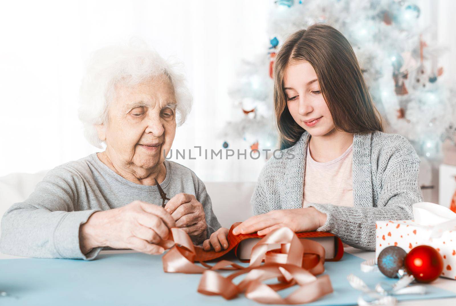 Smiling grandmother with granddaughter decorating gifts with purple paper together at Christmas
