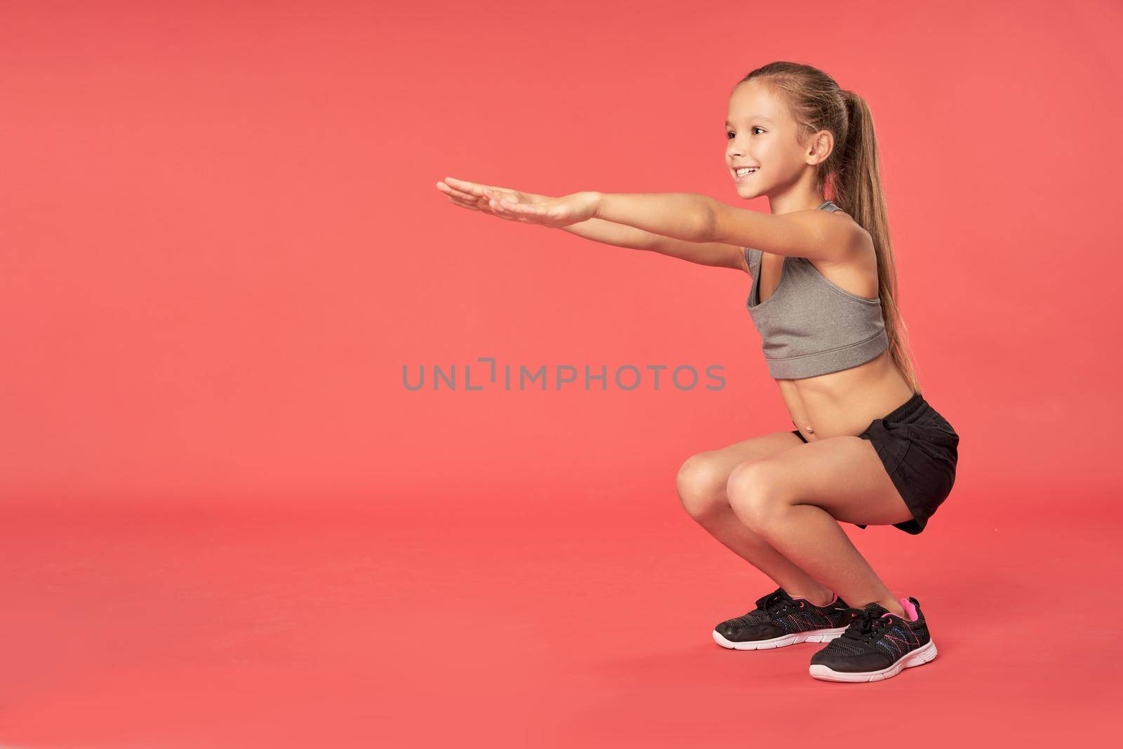 Cheerful sporty girl looking away and smiling while doing exercise against red background