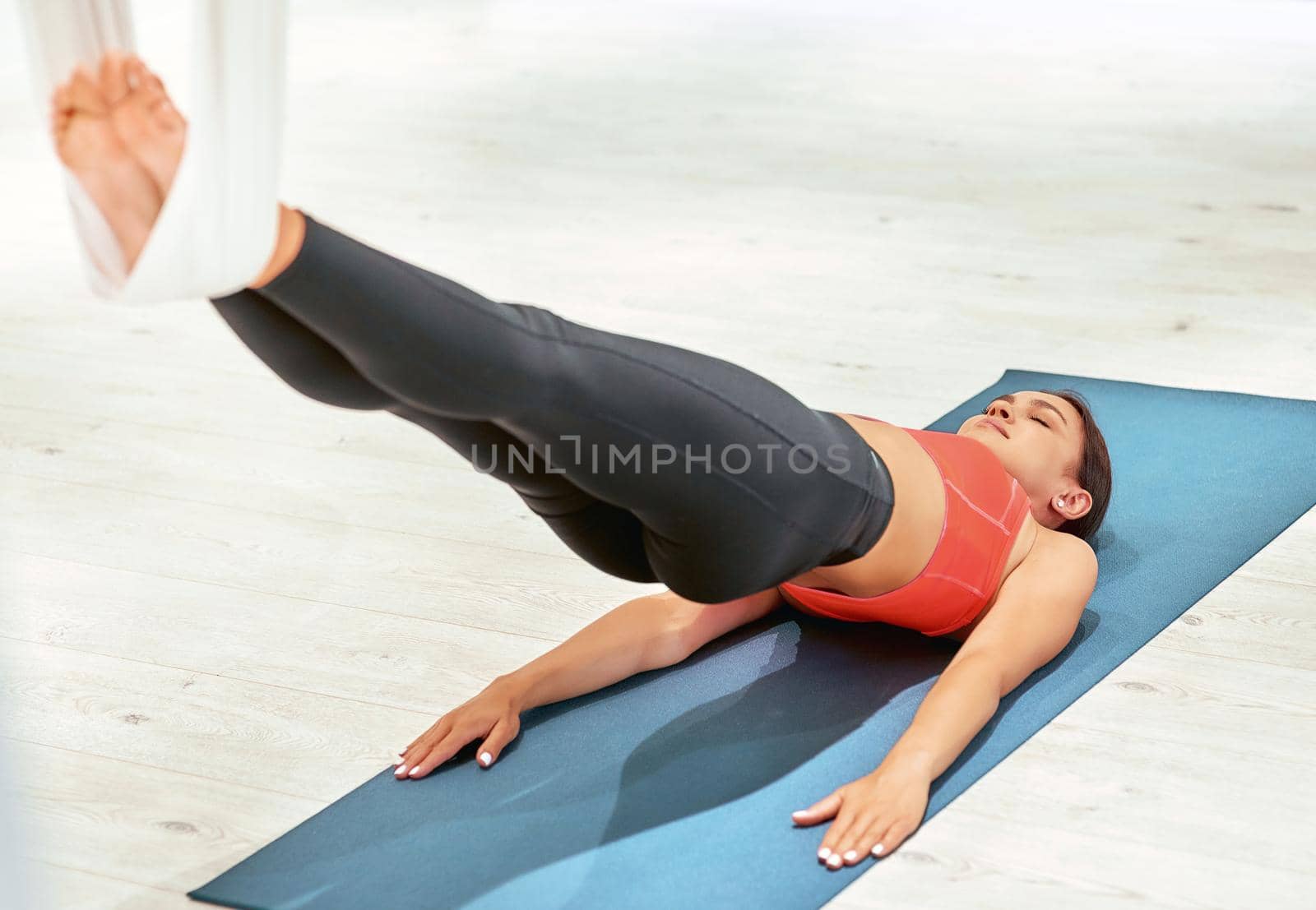 Young sportive woman lying on yoga mat in studio and doing sport exercises, practicing fly yoga by friendsstock