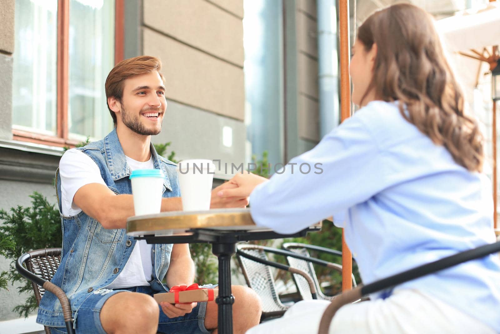 Smiling young girl having a date with her boyfriend at the coffee shop, man holding present box