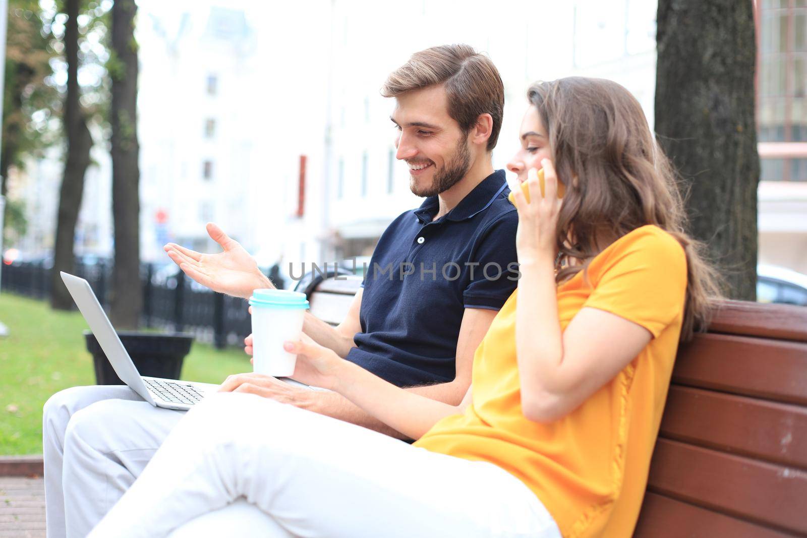 Attrative young couple using laptop computer while sitting on a bench outdoors