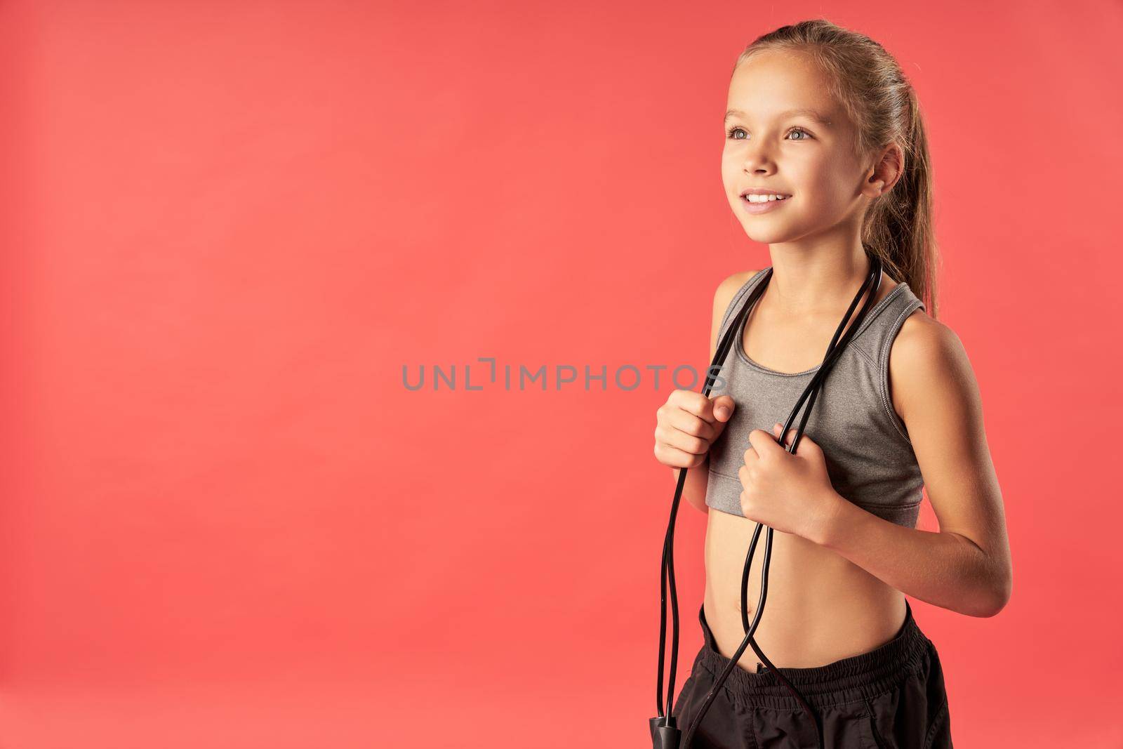 Cheerful cute girl in sportswear looking away and smiling while holding jump rope