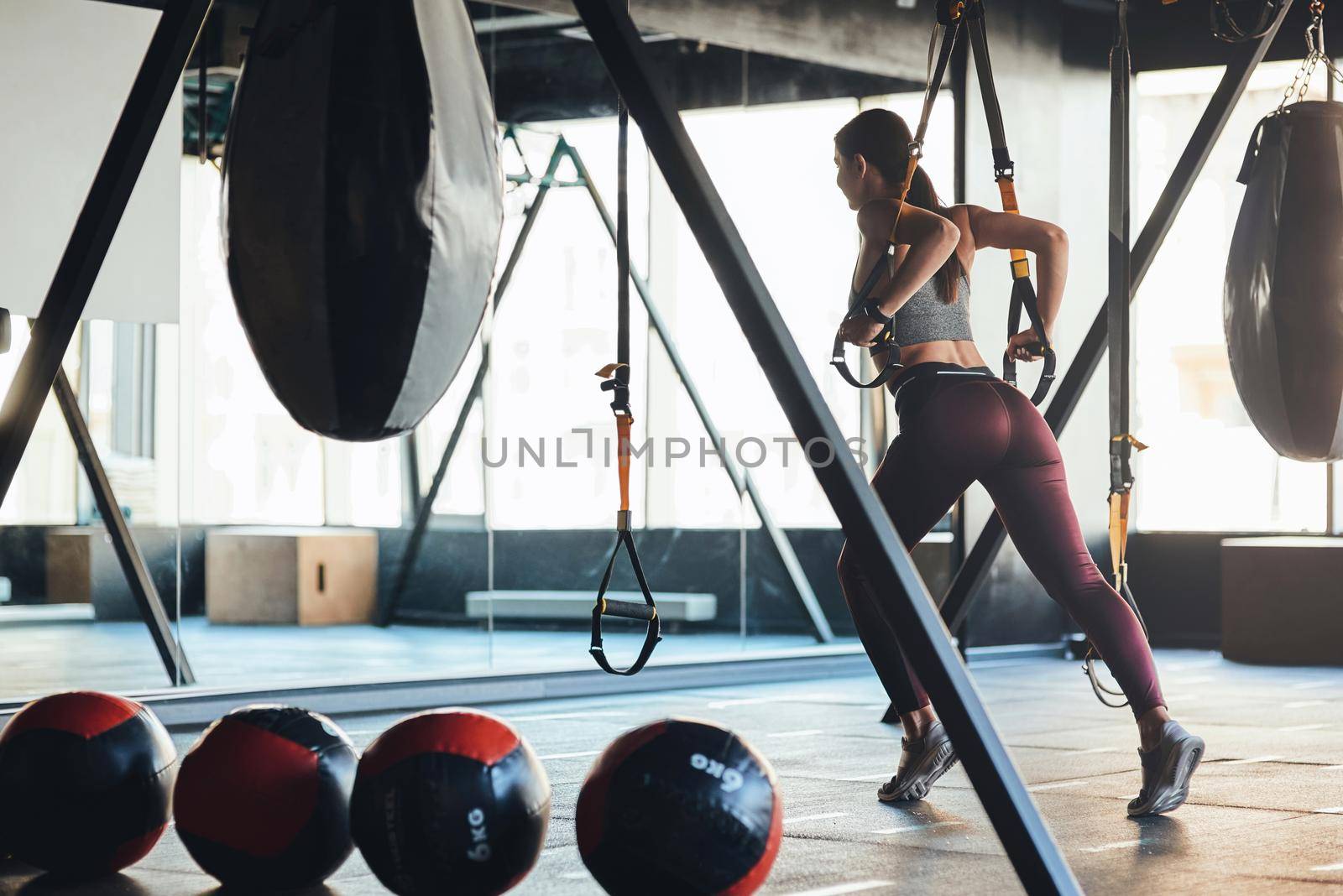 Young athletic woman with beautiful body wearing sports clothes exercising with fitness trx straps at gym by friendsstock