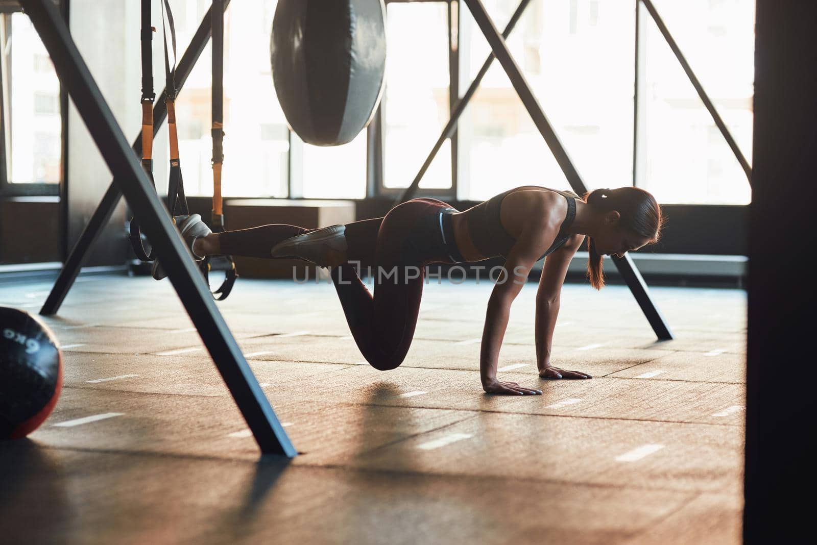 Suspension Training. Side view of young caucasian fitness woman in sportswear doing TRX workout at industrial gym, working out with fitness straps by friendsstock