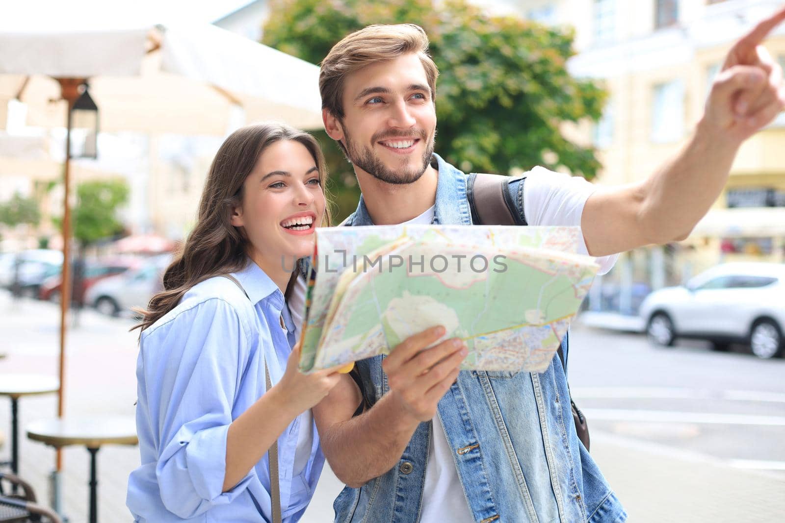 Beautiful young couple holding a map and smiling while standing outdoors. by tsyhun