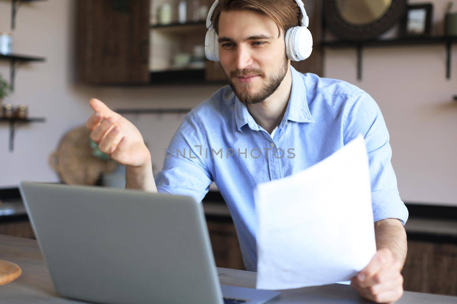 Smiling businessman greeting colleagues in video conference and negotiating distantly from home