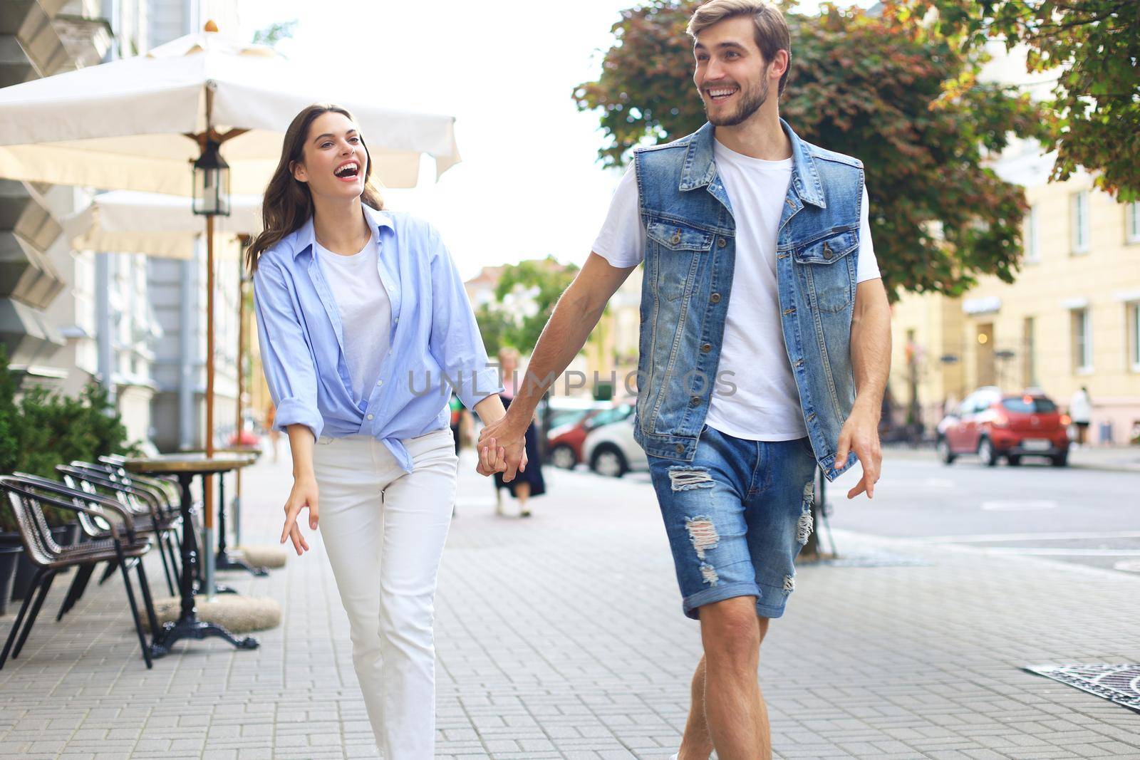 Image of lovely happy couple in summer clothes smiling and holding hands together while walking through city street