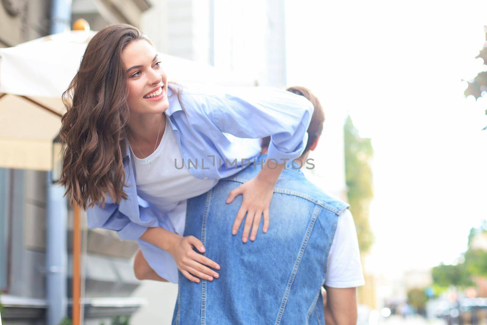 Handsome young man carrying young attractive woman on shoulders while spending time together outdoors