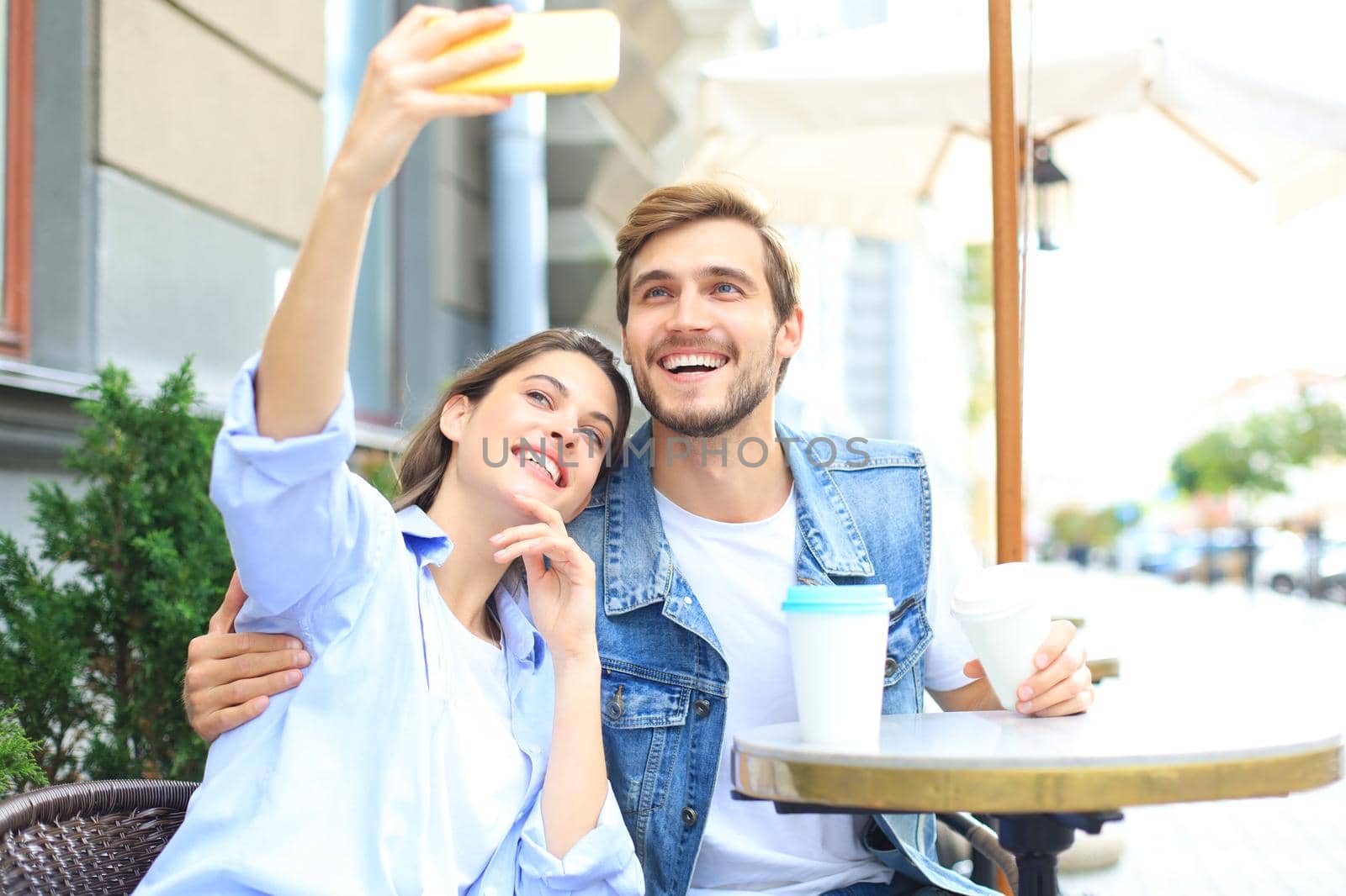 Beautiful young loving couple bonding to each other in cafe while woman making selfie by smart phone