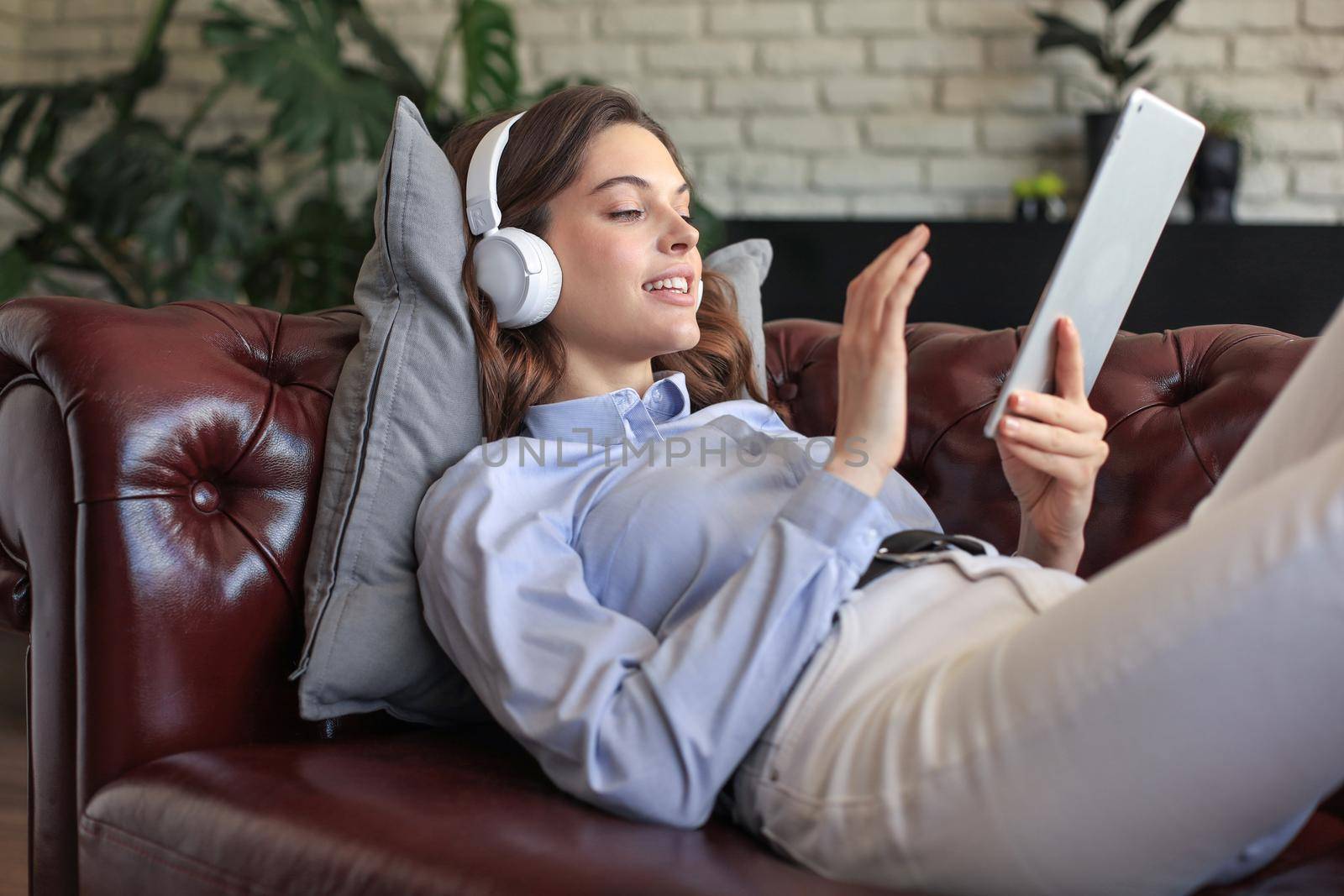 Smiling young woman with headphones and digital tablet on the sofa