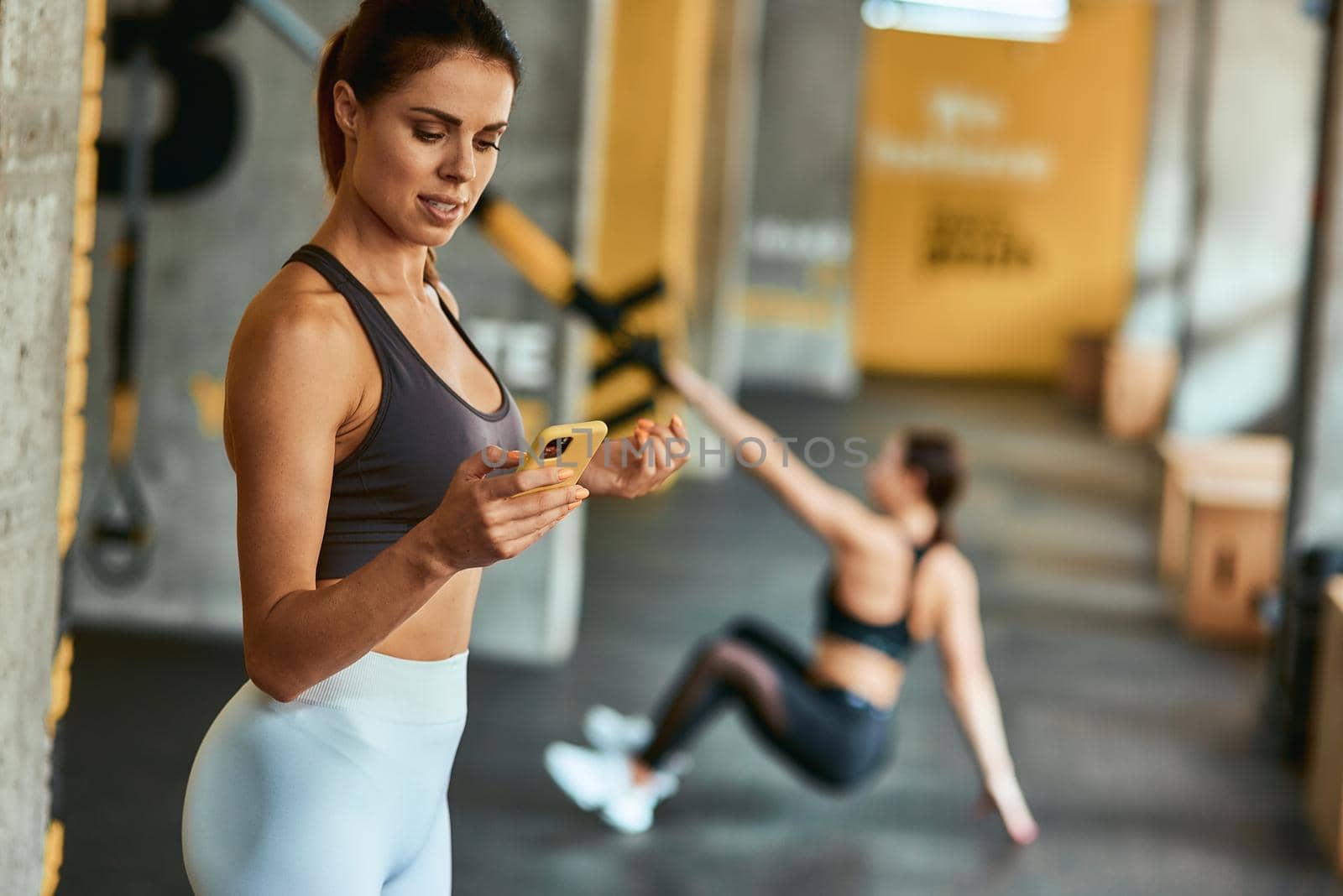 Young focused sportive woman using smartphone while exercising at gym. Sport, wellness and healthy lifestyle