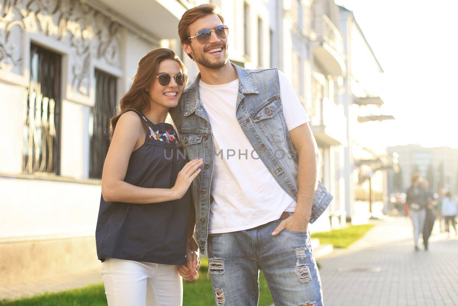 Image of lovely happy couple in summer clothes smiling and holding hands together while walking through city street