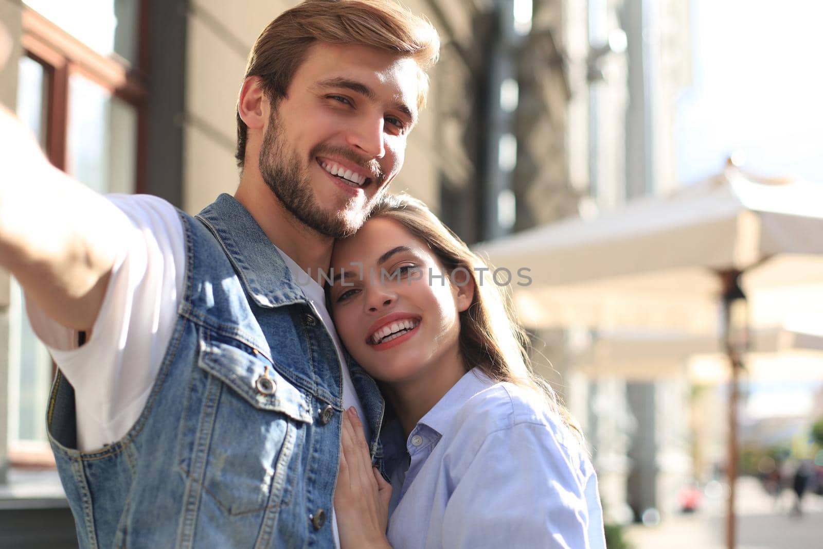 Beautiful lovely young couple walking at the city streets, hugging while taking a selfie