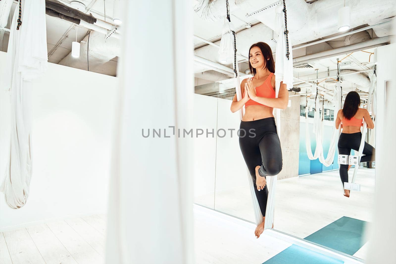 Harmony living. Young caucasian woman in sportswear practicing fly or aerial yoga in studio or gym, standing on the one leg in white hammock and meditating by friendsstock