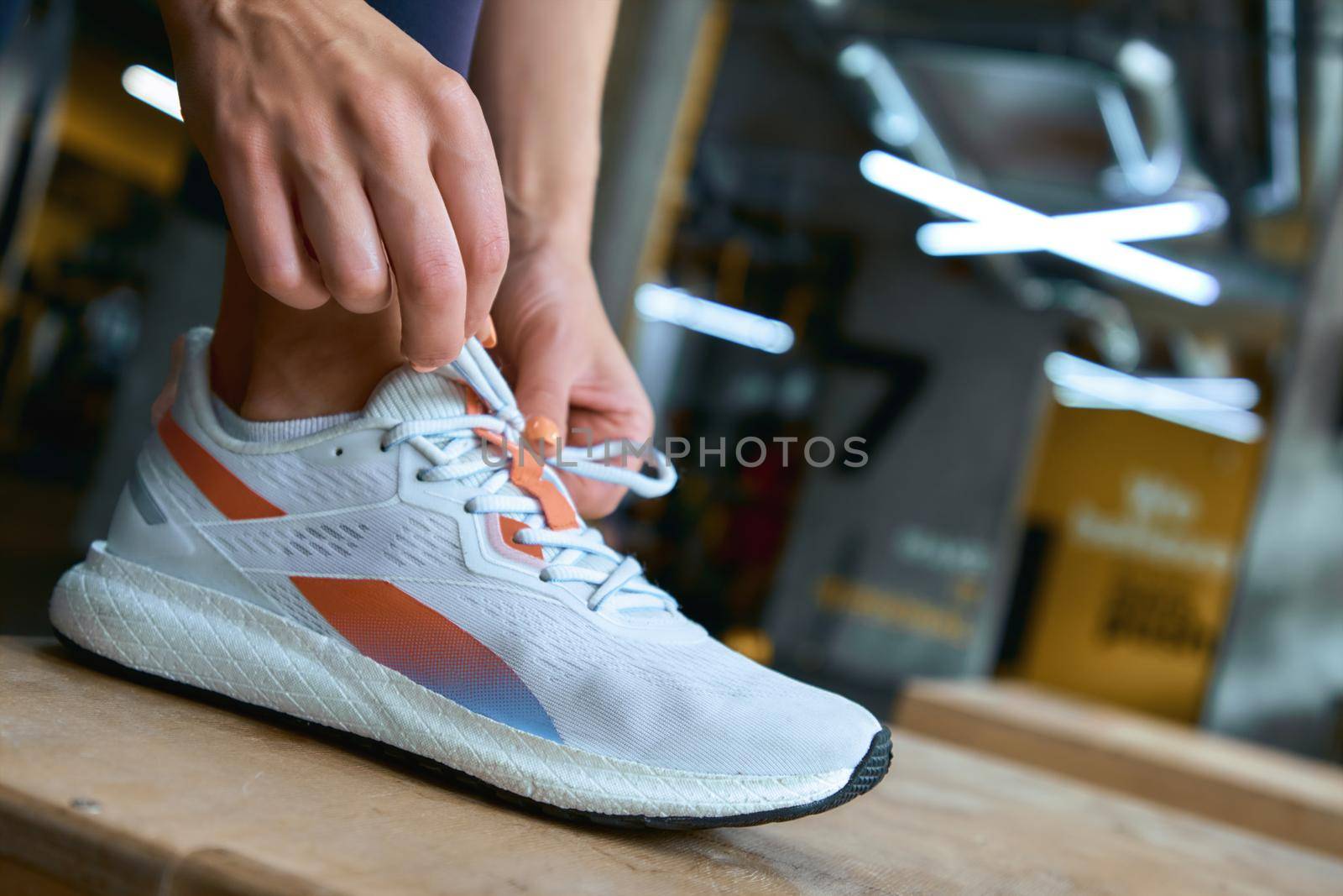 Cropped shot of a woman tiying shoelaces while exercising at gym. Sport, wellness and healthy lifestyle
