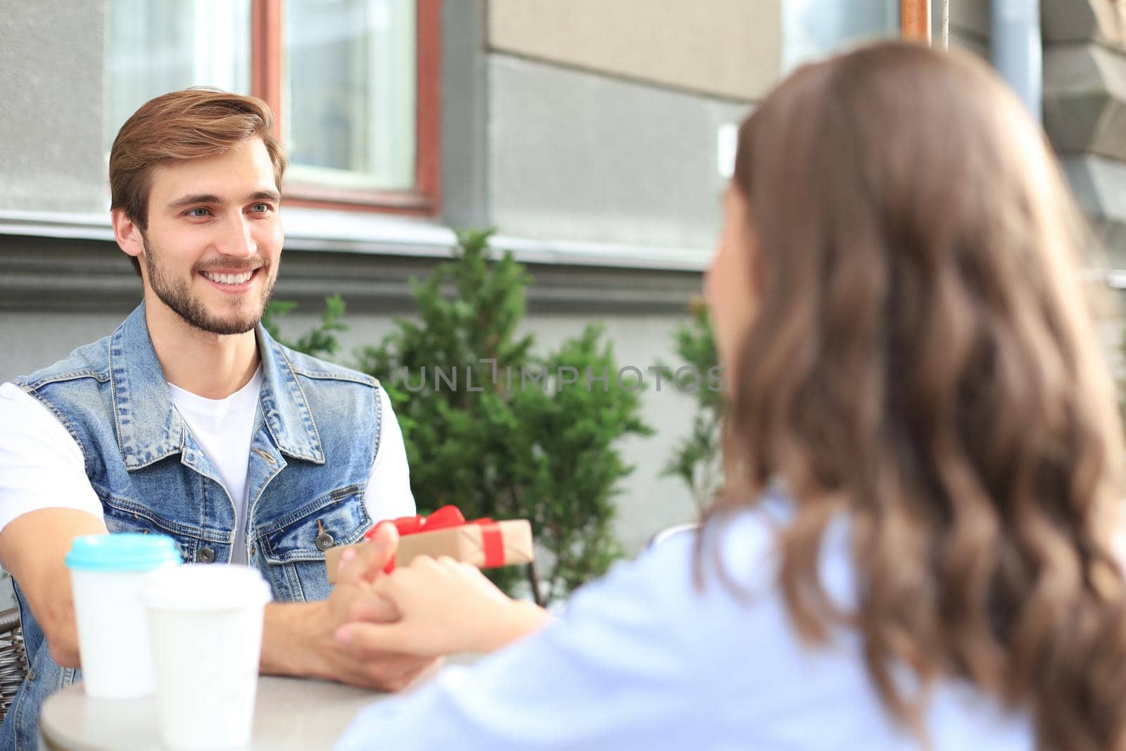 Smiling young girl having a date with her boyfriend at the coffee shop, man holding present box