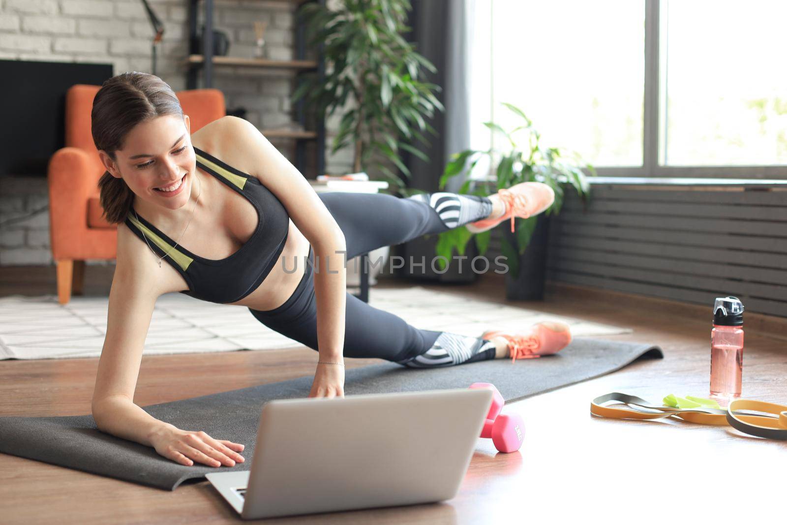 Fitness beautiful slim woman doing side plank and watching online tutorials on laptop, training in living room. Stay at home activities.